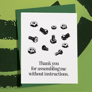 May include: A white greeting card with a green envelope. The card features a black and white illustration of nuts and bolts. The text reads, "Thank you for assembling me without instructions."