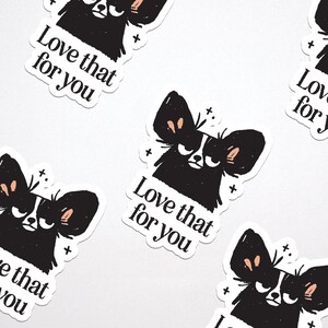 May include: A collection of white stickers featuring a black and white illustration of a dog with large ears and the text "Love that for you." The dog has a grumpy expression. Small plus signs are scattered around the dog.