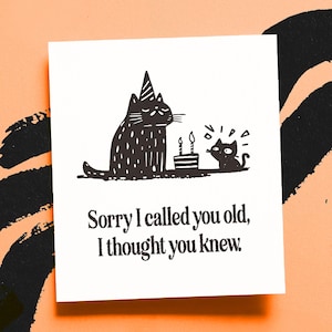 May include: A white greeting card with a black illustration of two cats and a birthday cake. The larger cat wears a party hat. The text reads, "Sorry I called you old, I thought you knew."