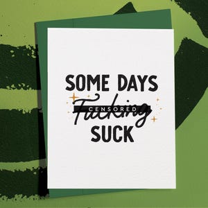 May include: A white greeting card with the text "SOME DAYS F*CKING SUCK" in black, with the word "F*CKING" censored. The card is inside a green envelope, with a green background.