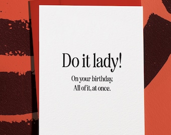 Può includere: Un biglietto di auguri bianco con il testo "Do it lady! On your birthday. All of it, at once." in nero. Il biglietto è posto su uno sfondo rosso con una busta rossa abbinata.