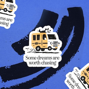 May include: A sticker featuring a yellow and white van with a dog on top. The van has a mailbox symbol and the text "Some dreams are worth chasing" on a white background. The background is blue with black brush strokes.