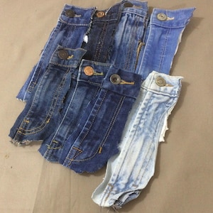 May include: A collection of denim jean pocket flaps in various shades of blue. Each flap features a button closure and visible stitching details. The arrangement showcases different washes and textures of the denim material.