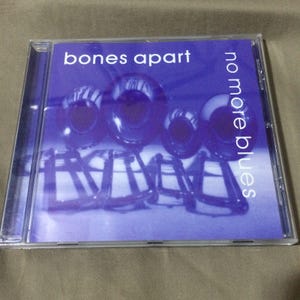 May include: A clear plastic CD jewel case featuring a purple cover with the text bones apart and no more blues. The artwork displays a graphic illustration of four trombone bells and their corresponding slide sections in a dark purple tone.