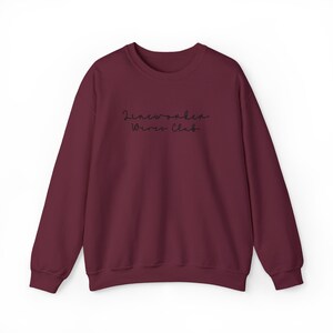May include: A maroon crewneck sweatshirt with the text "Lineworker Wives Club" in a delicate, handwritten font across the chest. The long-sleeved top is made of a soft material and is suitable for casual wear.