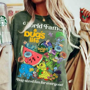 May include: A green t-shirt with a graphic of characters from the movie "A Bug's Life". The graphic includes a watermelon, flowers, and the text "A World Famous Bug's Life" and "Bug-sized fun for everyone!"
