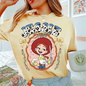 May include: A yellow t-shirt with a cartoon image of Jessie from Toy Story. The text "Jessie Cowgirl" is printed on the shirt in a black and white cow print.