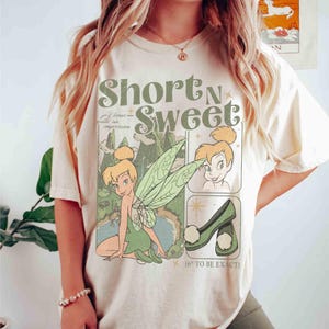 Könnte beinhalten: Cremefarbenes T-Shirt mit einer Grafik von Tinkerbell und dem Text "Short N Sweet". Das Design beinhaltet ein Cartoon-Bild von Tinkerbell, ihre Schuhe und den Satz "I leave quite an impression".