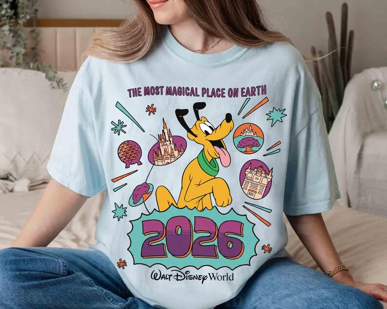 May include: Pale blue t-shirt with a Disney World design. It features Pluto, the text "THE MOST MAGICAL PLACE ON EARTH", and the year "2026". Various Disney park icons and the Walt Disney World logo are also present.