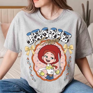 May include: Gray t-shirt with a cartoon image of Jessie from Toy Story. The image is surrounded by a floral design and the text "Jessie Cowgirl".