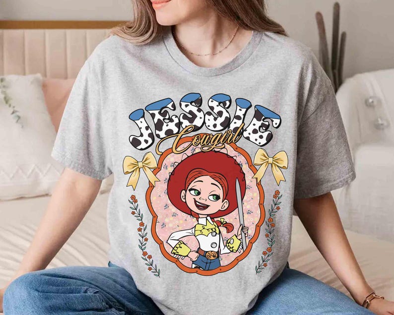 May include: Gray t-shirt with a cartoon image of Jessie from Toy Story. The image is surrounded by a floral design and the text "Jessie Cowgirl".