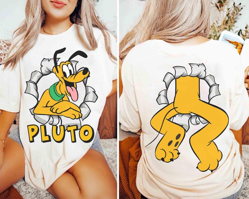 May include: Cream-coloured t-shirt with a cartoon Pluto graphic. The front shows Pluto emerging from a torn circle, with the name "PLUTO" below. The back displays Pluto's legs and paws. A fun, playful design.