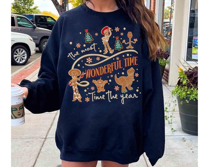 Puede incluir: Sudadera azul marino con un dise&ntilde;o festivo con personajes de dibujos animados y el texto "the most wonderful time of the year". El dise&ntilde;o incluye un &aacute;rbol de Navidad, un vaquero, un extraterrestre y un dinosaurio.