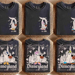 May include: Six dark grey t-shirts with Halloween-themed Disney designs. The shirts feature Mickey and Minnie Mouse dressed as ghosts, holding pumpkins. Some shirts have the Disneyland logo and the text "est. 1955".