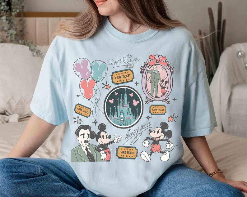 Peut inclure: T-shirt bleu clair avec un motif graphique color&eacute; repr&eacute;sentant Mickey Mouse, un ch&acirc;teau, des ballons et des billets de parc. Le motif comprend le texte "Walt Disney" et "Mickey Mouse" dans un style fantaisiste.