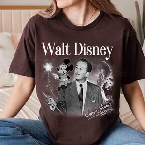 Puede incluir: Una camiseta de manga corta de color marr&oacute;n oscuro con un gr&aacute;fico de estilo vintage de Walt Disney en traje y corbata, con Mickey Mouse sobre su hombro. El texto Walt Disney aparece en blanco sobre el gr&aacute;fico, con una firma en la parte inferior.