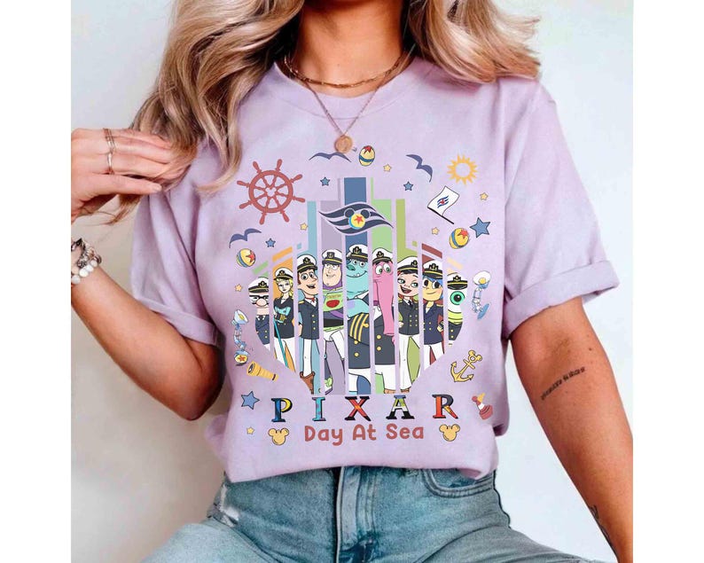K&ouml;nnte beinhalten: Ein lilafarbenes T-Shirt mit einer Grafik von Pixar-Charakteren in Matrosenuniformen. Das Design umfasst ein Steuerrad, Sterne und den Text "PIXAR Day At Sea" in bunten Buchstaben. Das Shirt hat hochgekrempelte &Auml;rmel.