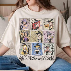 May include: A cream-coloured t-shirt featuring a grid of nine cartoon princesses dressed as witches, with bats and spiderwebs. The text "Walt Disney World" is printed at the bottom. The shirt has a relaxed fit.