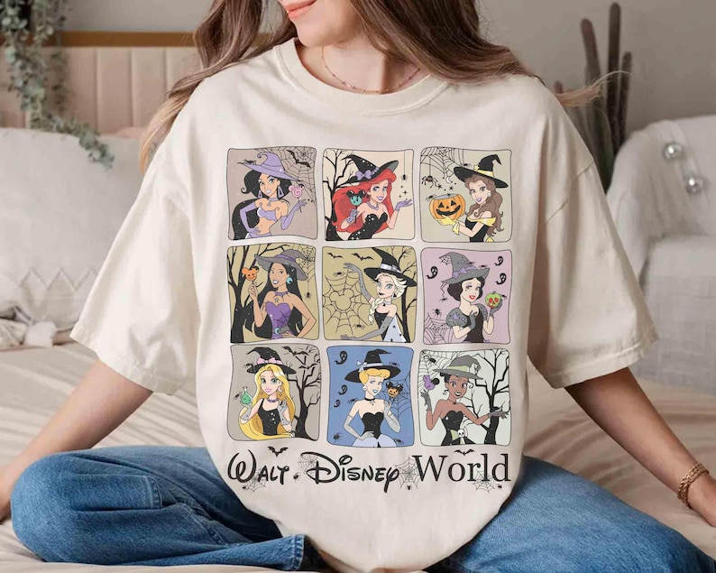 May include: A cream-coloured t-shirt featuring a grid of nine cartoon princesses dressed as witches, with bats and spiderwebs. The text "Walt Disney World" is printed at the bottom. The shirt has a relaxed fit.