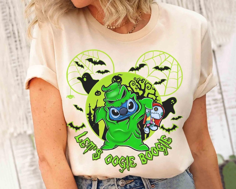 May include: Cream-colored t-shirt featuring a green cartoon character resembling Stitch, dressed as Oogie Boogie, holding a rag doll. The design includes bats, ghosts, and the text "Let's Oogie Boogie" in green, set against a Halloween-themed background.