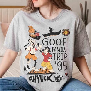 Pode incluir: Camiseta cinza claro com um desenho animado do Pateta e Max. O design inclui o texto "GOOF FAMILY TRIP '95" e "AHYUCK". A camiseta tem gola redonda e mangas curtas. Perfeita para os f&atilde;s da Disney.