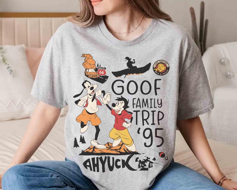 Pode incluir: Camiseta cinza claro com um desenho animado do Pateta e Max. O design inclui o texto "GOOF FAMILY TRIP '95" e "AHYUCK". A camiseta tem gola redonda e mangas curtas. Perfeita para os f&atilde;s da Disney.