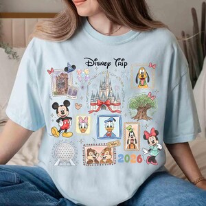 Puede incluir: Camiseta azul claro con un dise&ntilde;o de Disney. El dise&ntilde;o presenta personajes de Disney como Mickey, Donald y Minnie, as&iacute; como el texto "Disney Trip 2026".