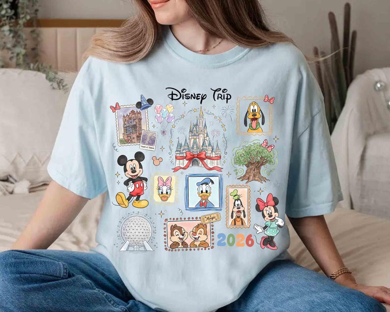 Puede incluir: Camiseta azul claro con un dise&ntilde;o de Disney. El dise&ntilde;o presenta personajes de Disney como Mickey, Donald y Minnie, as&iacute; como el texto "Disney Trip 2026".