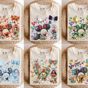 May include: Cream-colored t-shirts with colorful graphic designs featuring cartoon characters, bows, and decorative elements. Each shirt showcases a different character theme, with detailed illustrations and vibrant colors.