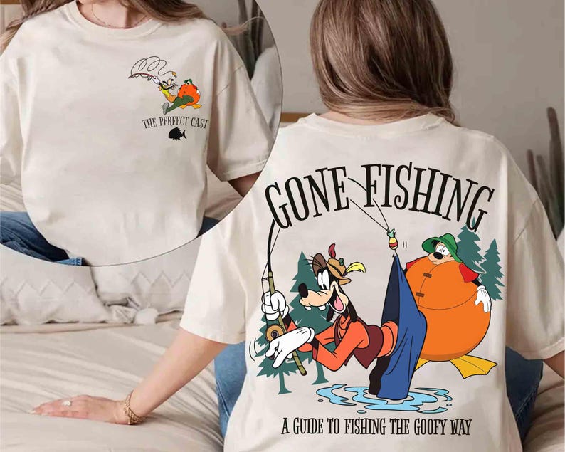 May include: Cream-colored t-shirt featuring a cartoon graphic of Goofy fishing. The front of the shirt has a small graphic with the text "THE PERFECT CAST". The back of the shirt has a larger graphic with the text "GONE FISHING" and "A GUIDE TO FISHING THE GOOFY WAY".