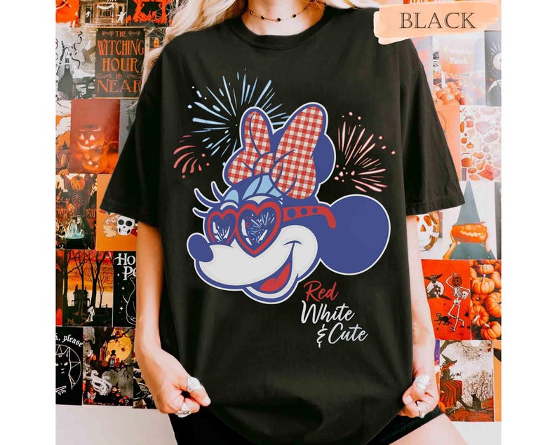 Op de afbeelding: Zwart T-shirt met een cartoonfiguur in rood, wit en blauw, inclusief hartvormige zonnebril en een strik. De tekst "Red White & Cute" is ook zichtbaar.