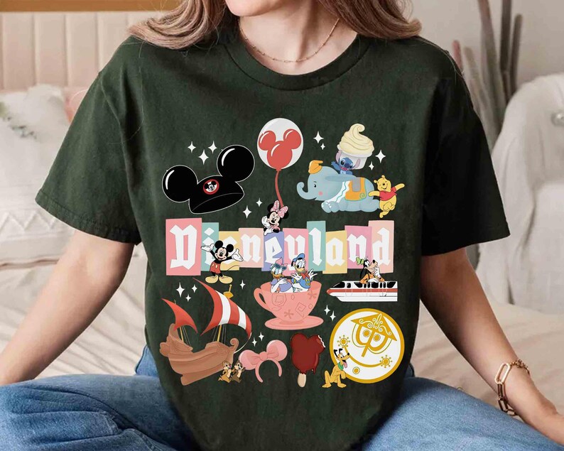May include: Dark green t-shirt featuring a colorful Disneyland graphic. The design includes Mickey Mouse ears, Minnie Mouse, Dumbo, Winnie the Pooh, and other iconic Disney characters. The word "Disneyland" is prominently displayed.