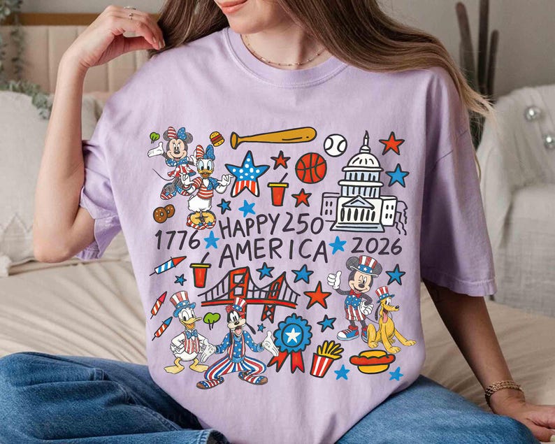 Puede incluir: Una camiseta de color lila claro con un gr&aacute;fico colorido de personajes de dibujos animados y s&iacute;mbolos patri&oacute;ticos. El dise&ntilde;o incluye a Mickey y Minnie Mouse, el Pato Donald y Pluto, con el texto "Happy 250 America 2026" y el a&ntilde;o "1776".