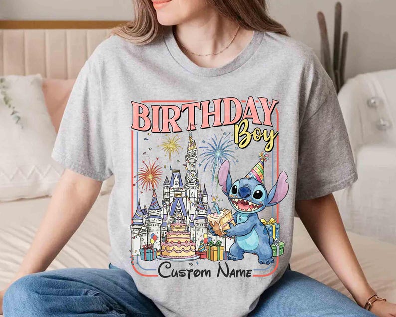 May include: A gray t-shirt featuring a colorful graphic with the text "BIRTHDAY Boy" and "Custom Name". The graphic includes a cartoon character, a castle, fireworks, a cake, and wrapped gifts.