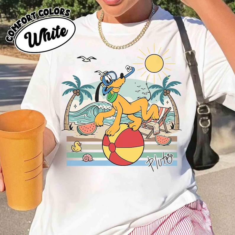 K&ouml;nnte beinhalten: Wei&szlig;es T-Shirt mit einer farbenfrohen Grafik von Pluto auf einem Strandball, der einen Schnorchel tr&auml;gt. Das Design zeigt eine Strandszene mit Palmen, Wellen und einer Sonne. Der Text "COMFORT COLORS White" befindet sich in einem wei&szlig;en Oval.