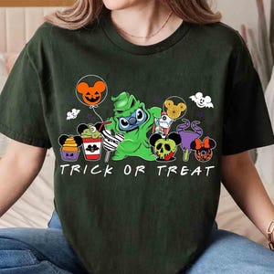May include: Dark green t-shirt with a Halloween-themed graphic. The design features a green character holding a balloon, surrounded by cartoon treats and the words "TRICK OR TREAT" in white. The shirt is a casual, short-sleeved style.