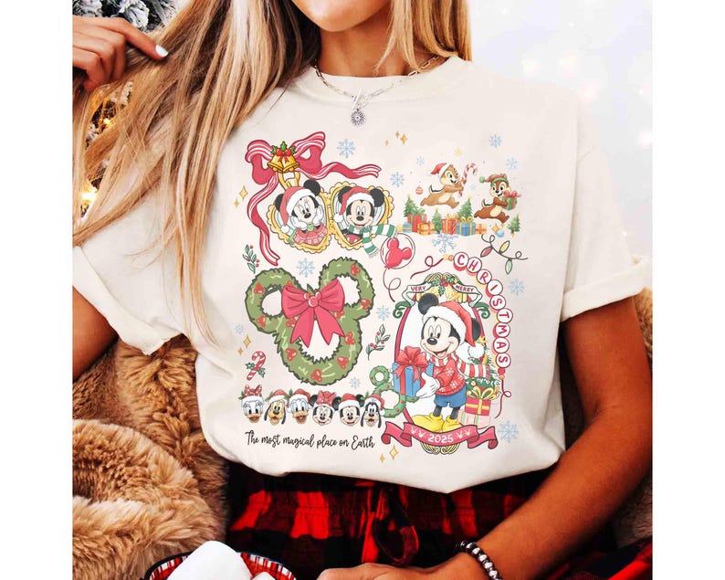 May include: Cream-colored t-shirt featuring a festive Christmas design with Mickey Mouse and friends. The graphic includes a Mickey Mouse-shaped wreath, the words "Christmas" and "2025", and the phrase "The most magical place on Earth".