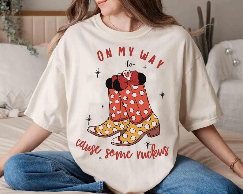 Peut inclure: T-shirt blanc avec un motif de bottes rouges et jaunes &agrave; pois blancs. Le texte "On my way to cause some ruckus" est imprim&eacute; sur le t-shirt.