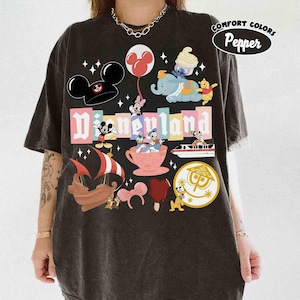 May include: Dark gray t-shirt featuring a colorful Disneyland graphic. The design includes Mickey Mouse ears, various Disney characters, and the Disneyland logo. The shirt has a vintage, distressed look with the words "Comfort Colors Pepper" printed on the upper right.