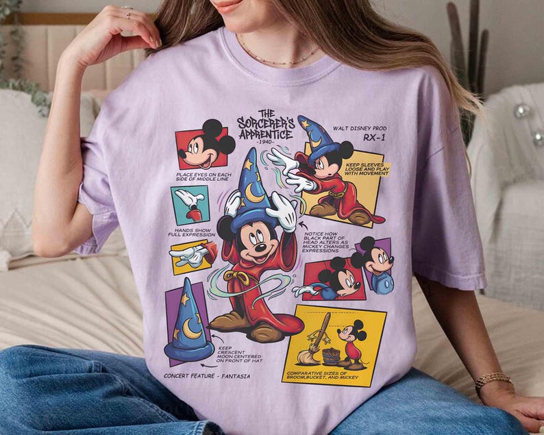 May include: A light purple t-shirt featuring a graphic of Mickey Mouse as the Sorcerer's Apprentice. The design includes multiple panels with illustrations and text from the 1940 Disney film, Fantasia.