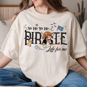Peut inclure: T-shirt cr&egrave;me avec un motif sur le th&egrave;me des pirates. Le design comprend le mot "PIRATE" dans une police stylis&eacute;e, un personnage de pirate de dessin anim&eacute; et la phrase "Life for me". Des illustrations suppl&eacute;mentaires sur le th&egrave;me des pirates, telles qu'une ancre, un drapeau et une longue-vue, sont &eacute;galement pr&eacute;sentes.