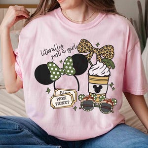 May include: Pink t-shirt with a graphic featuring a Minnie Mouse ear headband, a coffee cup, and sunglasses. The text "literally just a girl" is above the graphic. The design includes a park ticket.