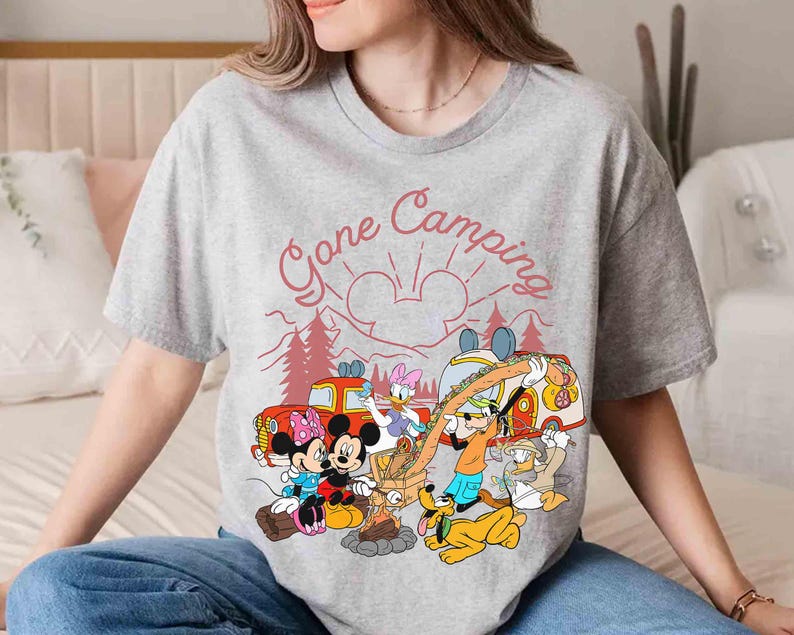 Pu&ograve; includere: T-shirt grigia con grafica a tema campeggio con Topolino, Minnie, Paperino, Paperina, Pippo e Pluto. La grafica include il testo "Gone Camping" in rosso, con un design di sole e montagne.