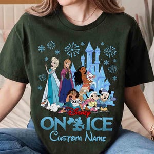 Puede incluir: Camiseta verde oscuro con los personajes de Disney Elsa, Anna, Moana, Mickey y Minnie Mouse frente a un castillo. El texto "ON ICE" y "Custom Name" est&aacute; impreso en azul. El dise&ntilde;o tambi&eacute;n incluye copos de nieve y fuegos artificiales.