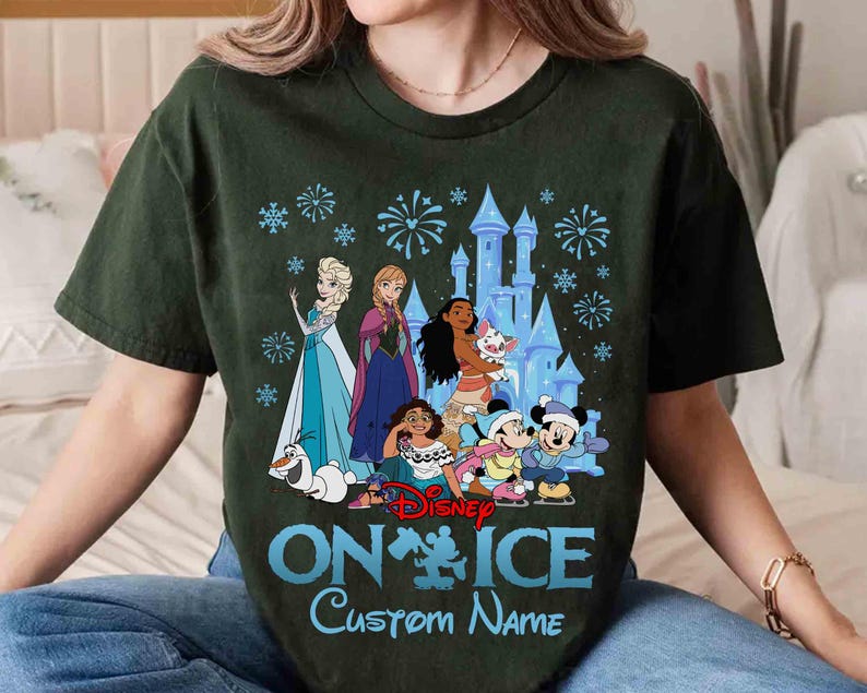 Puede incluir: Camiseta verde oscuro con los personajes de Disney Elsa, Anna, Moana, Mickey y Minnie Mouse frente a un castillo. El texto "ON ICE" y "Custom Name" est&aacute; impreso en azul. El dise&ntilde;o tambi&eacute;n incluye copos de nieve y fuegos artificiales.