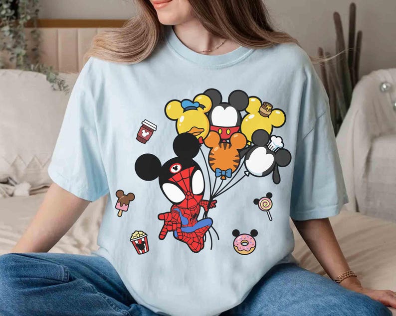 Puede incluir: Camiseta azul claro con un personaje de dibujos animados de Spider-Man sosteniendo globos con forma de Mickey Mouse y sus amigos. La camiseta tambi&eacute;n tiene gr&aacute;ficos de una taza de caf&eacute;, palomitas de ma&iacute;z, helado, una piruleta y una rosquilla.