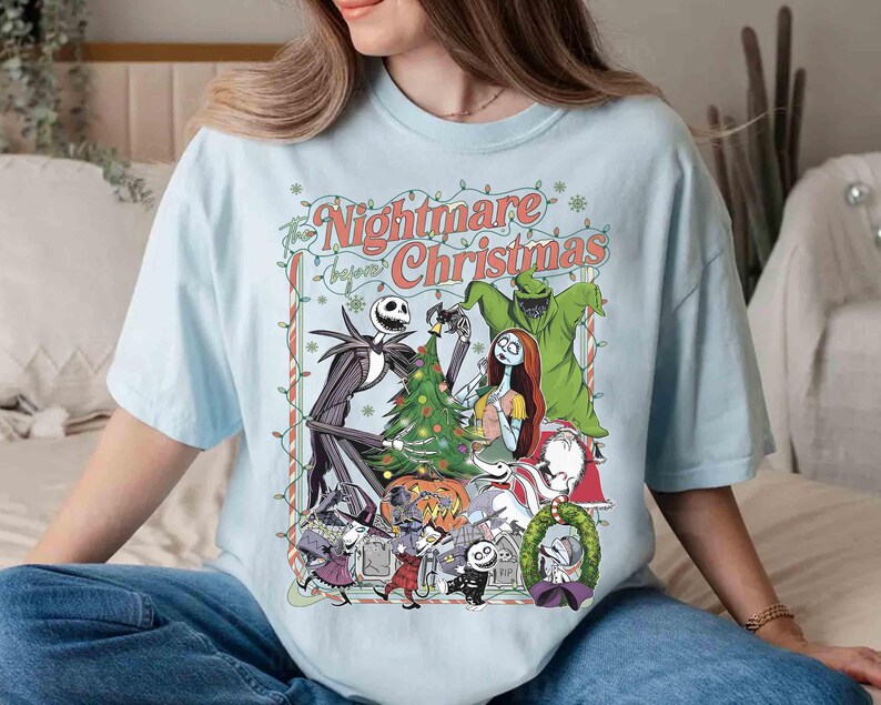 K&ouml;nnte beinhalten: Hellblaues T-Shirt mit einem Motiv aus "The Nightmare Before Christmas". Das Design zeigt Jack Skellington, Sally und andere Charaktere, mit dem Text "Nightmare Before Christmas". Das Shirt hat eine lockere Passform.