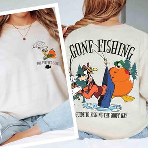 May include: Off-white sweatshirt featuring a cartoon design of Goofy fishing. The front of the shirt has the text "The Perfect Cast" and a small fish graphic. The back of the shirt says "Gone Fishing" and "Guide to Fishing the Goofy Way".