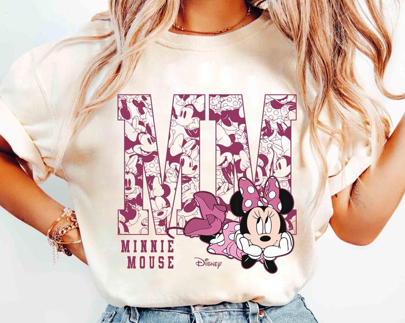 May include: Cream-colored t-shirt featuring a graphic of Minnie Mouse. The letters "MM" are filled with Minnie Mouse illustrations. Below the letters, the text reads "MINNIE MOUSE" and the Disney logo.