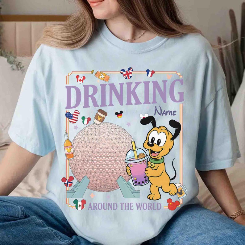 Puede incluir: Camiseta azul claro con un gr&aacute;fico que dice "DRINKING AROUND THE WORLD". El dise&ntilde;o incluye una esfera rosa, un personaje de dibujos animados e iconos de pa&iacute;ses. La camiseta est&aacute; hecha de un material suave.